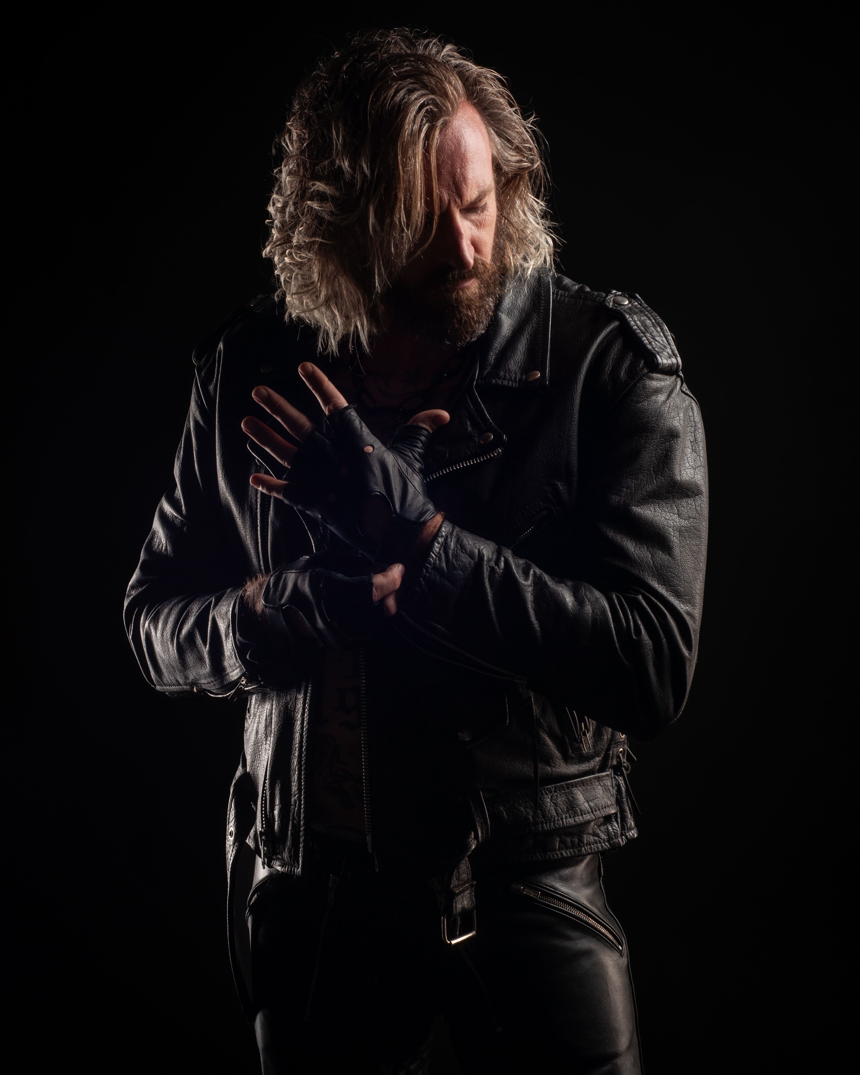 Kevin in a black leather jacket, direct gaze, low light